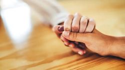 Close-up of two people holding hands across a table.
