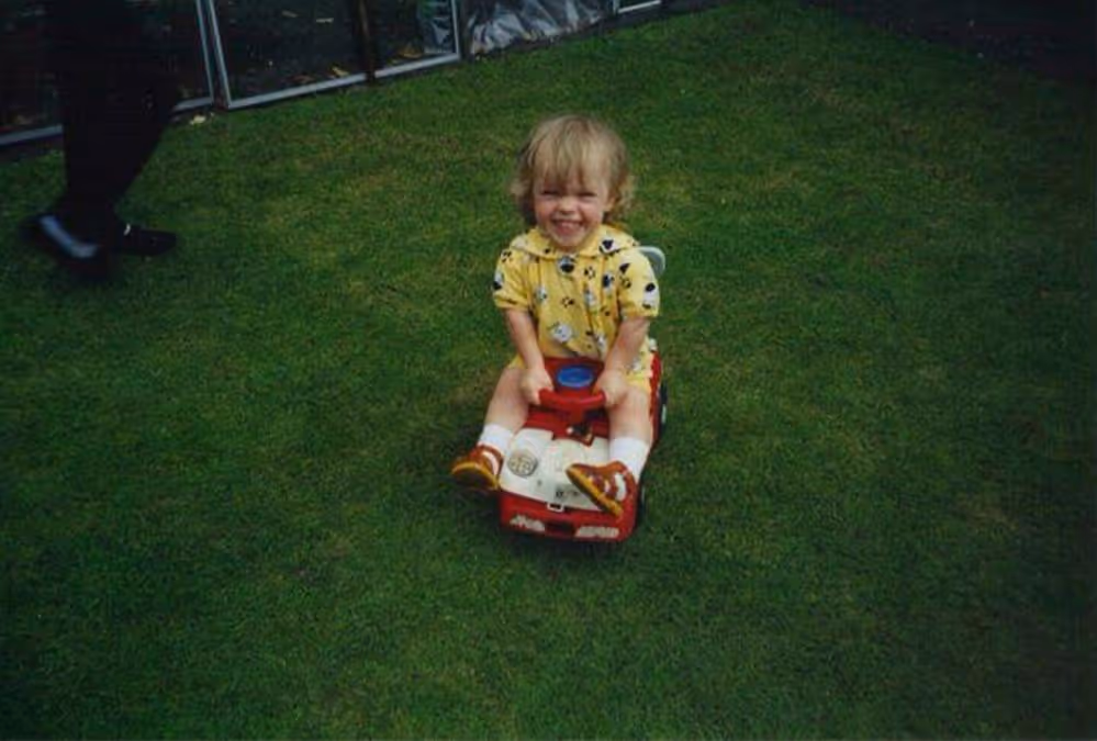 Ellie Simmonds in 1998 playing in a garden on a toy car. 