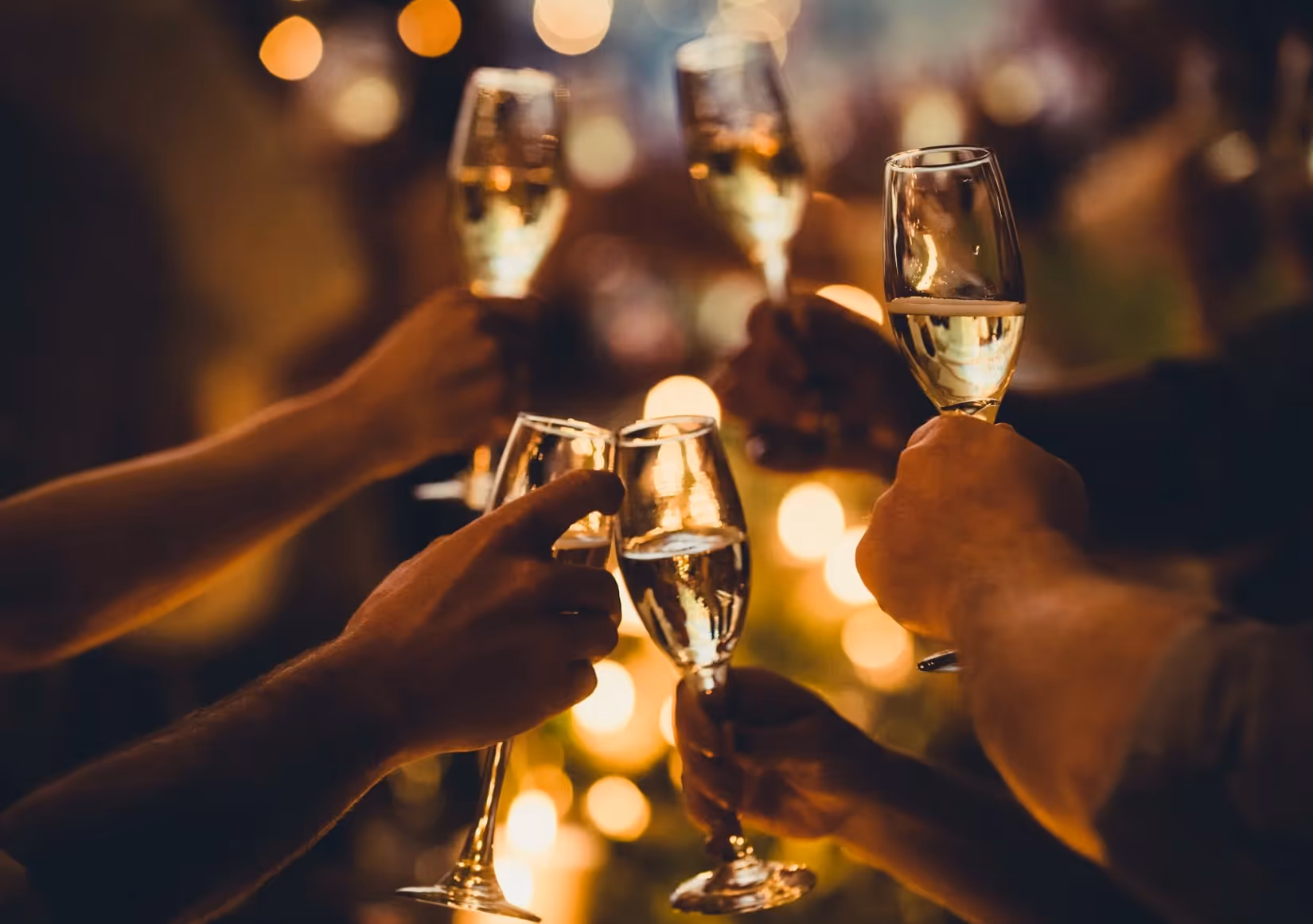People raising glasses of champagne in a warm, softly lit toast.